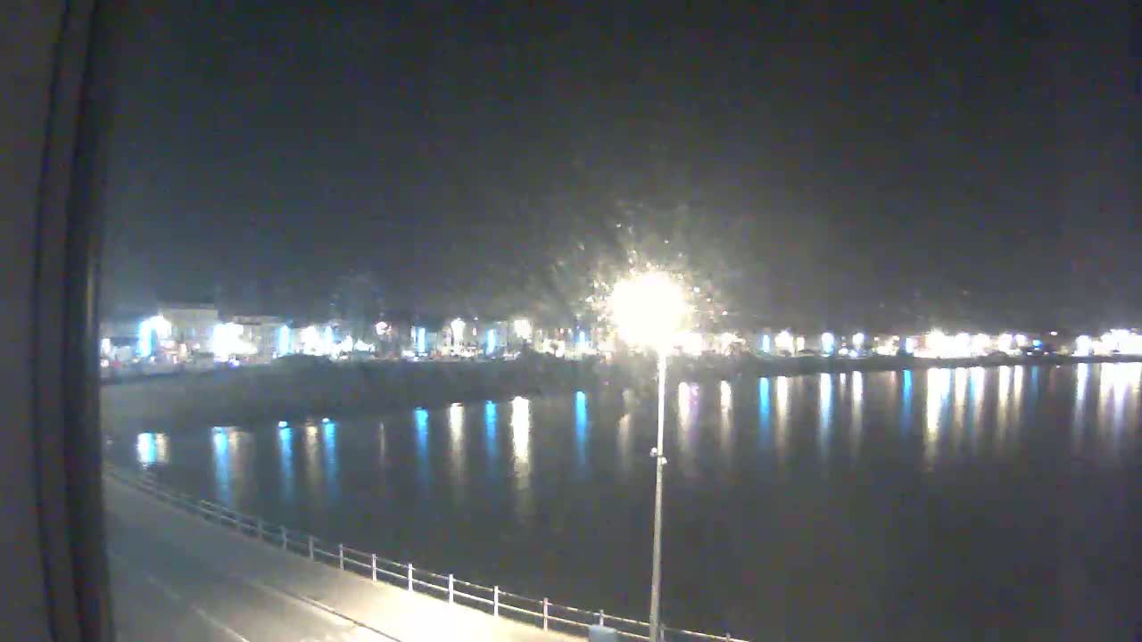 A nighttime view of a calm body of water reflecting the lights of a town across the water, seen from a slightly elevated position.
