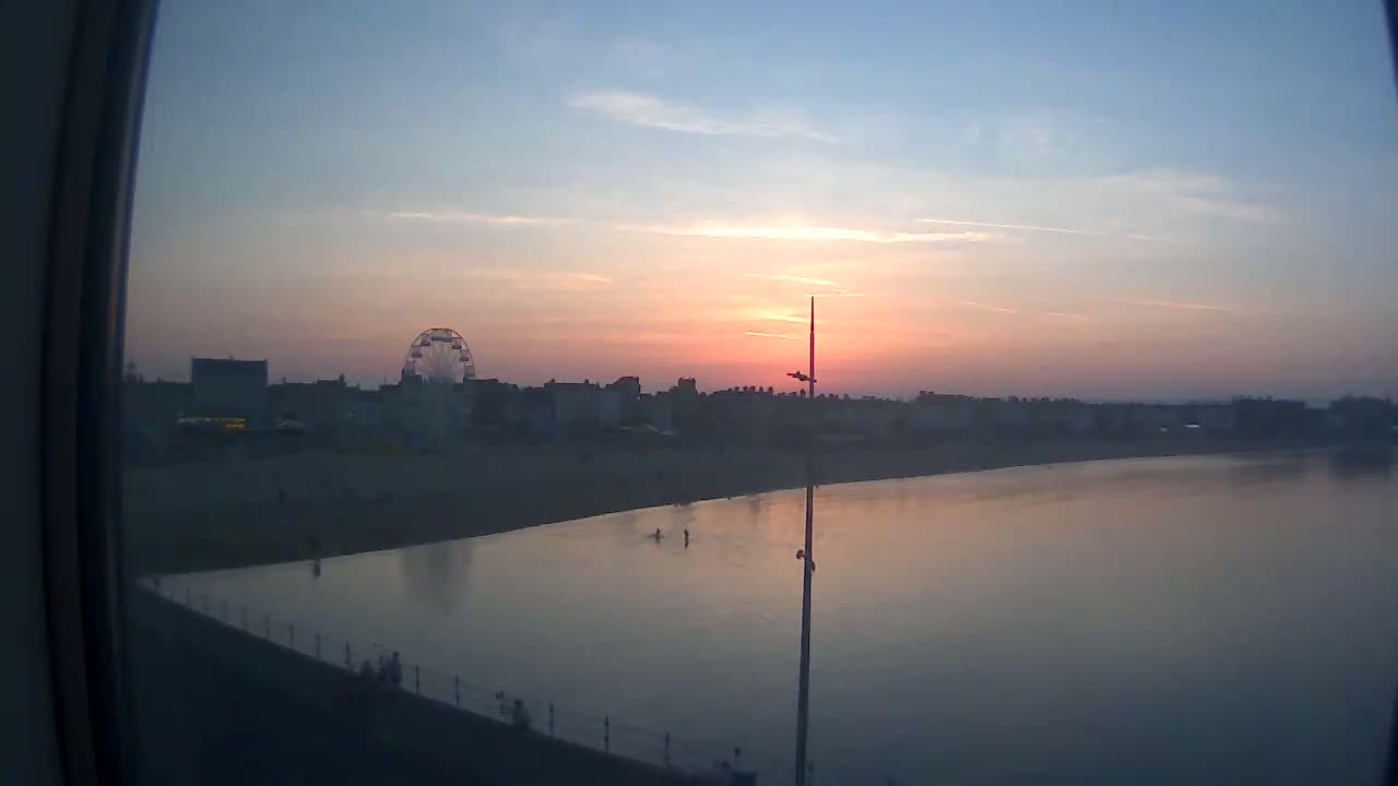 A sunset over a calm body of water, with a Ferris wheel and buildings visible on the shore.