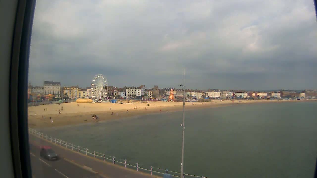 A sandy beach with a Ferris wheel and buildings behind it is seen under an overcast sky.