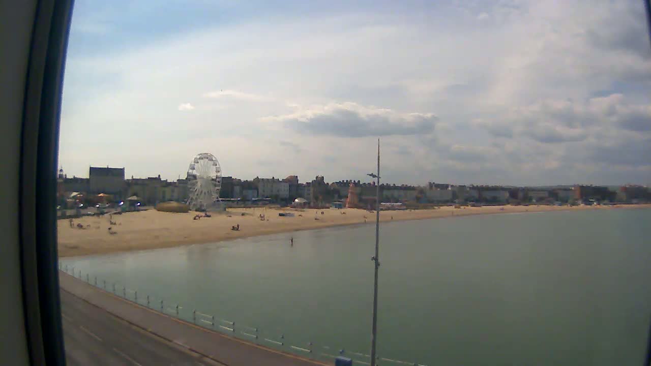 A sandy beach with a Ferris wheel and buildings in the background is visible on a partly cloudy day.