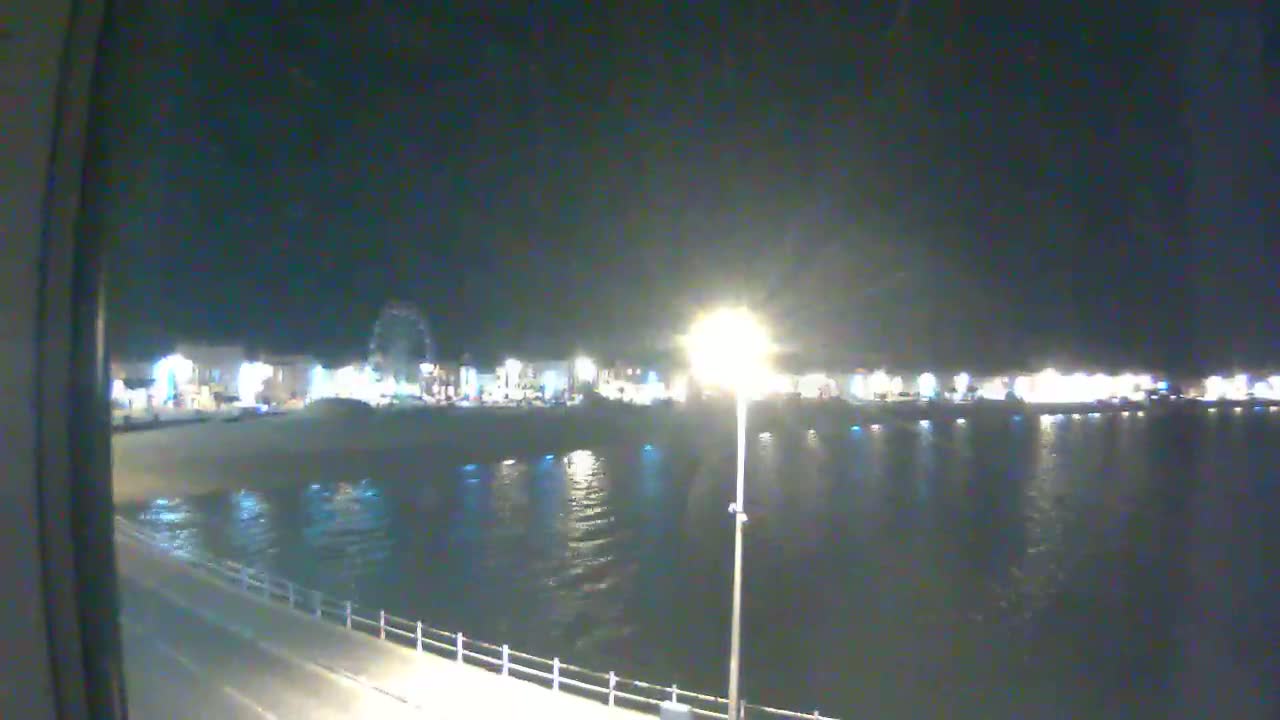 A nighttime view of a waterfront at night, showing a Ferris wheel and other illuminated buildings across a calm body of water.