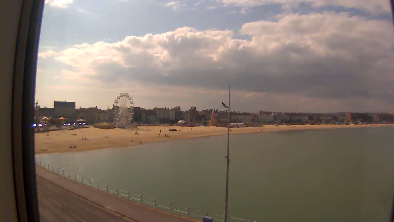 A partly cloudy day reveals a beach with a Ferris wheel and buildings in the background, seen from a slightly elevated vantage point.