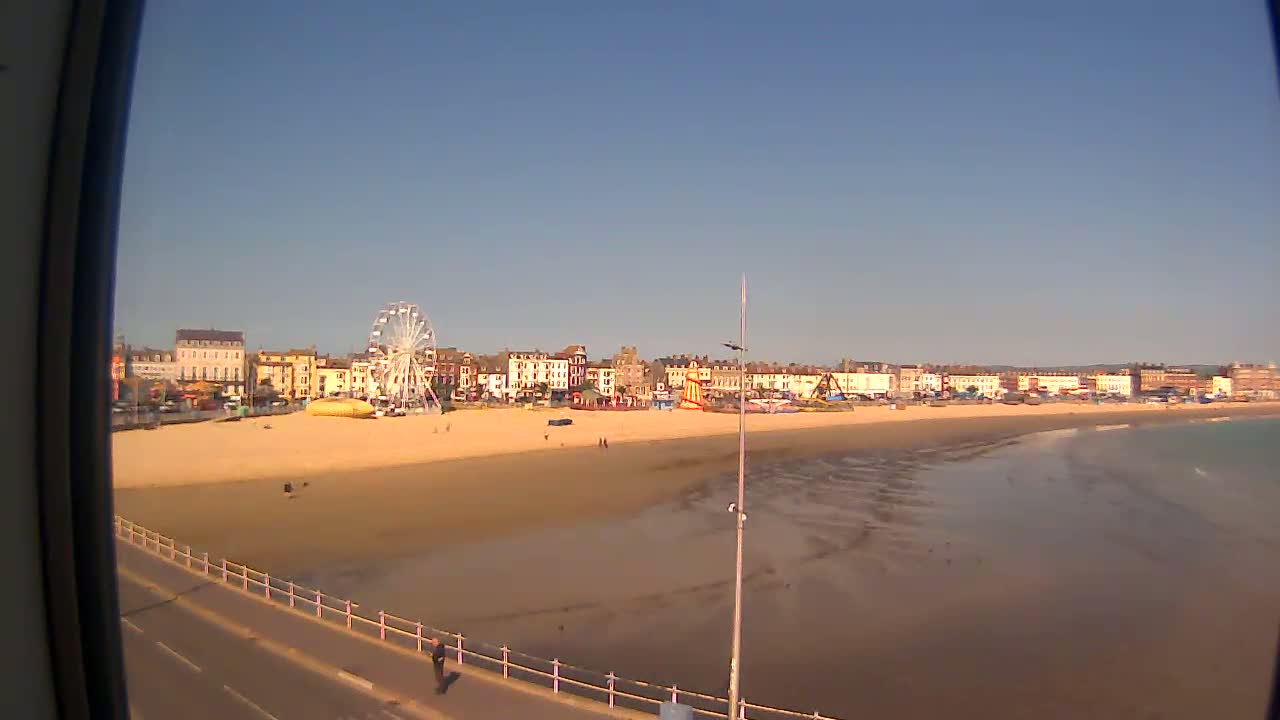 A sandy beach with a Ferris wheel and buildings behind it is viewed on a sunny day.