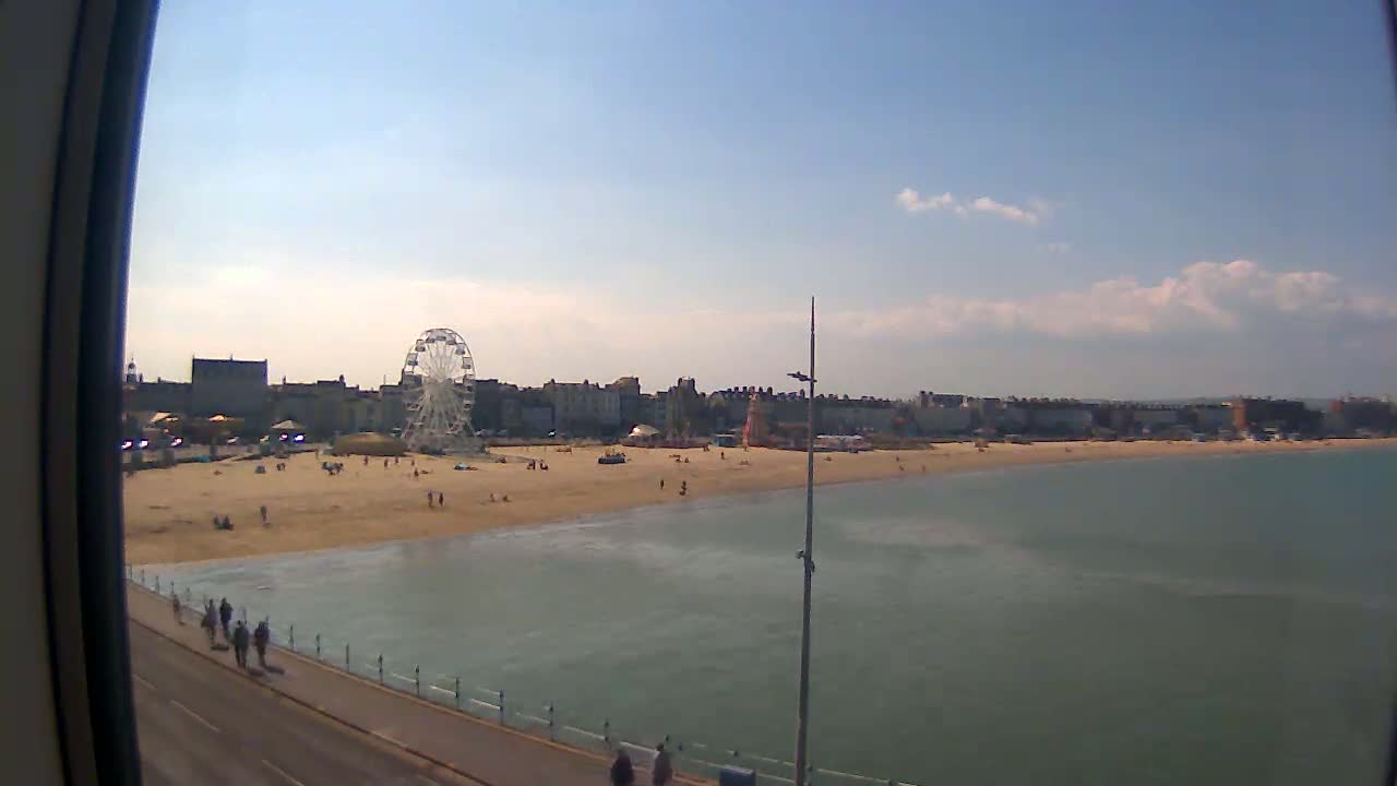 A Ferris wheel and beach with a few people on a sunny day.