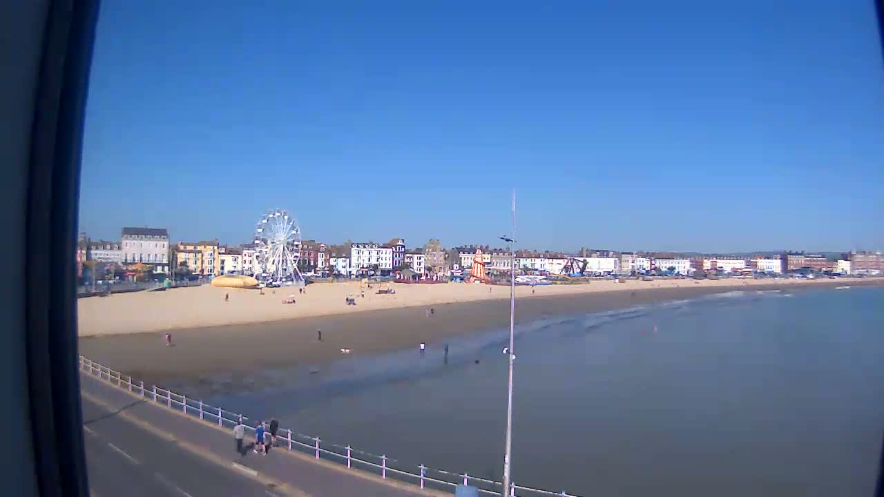 A sandy beach with a Ferris wheel and several buildings behind it stretches along a calm ocean under a clear blue sky.