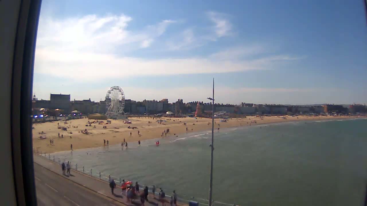 A sunny day at a beach with a Ferris wheel and many people on the sand and in the water.