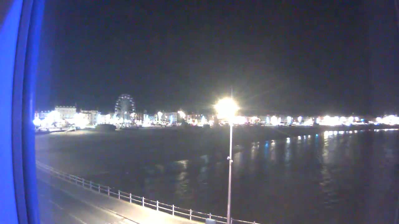 A nighttime view of a brightly lit waterfront with a Ferris wheel and calm water reflecting the lights.
