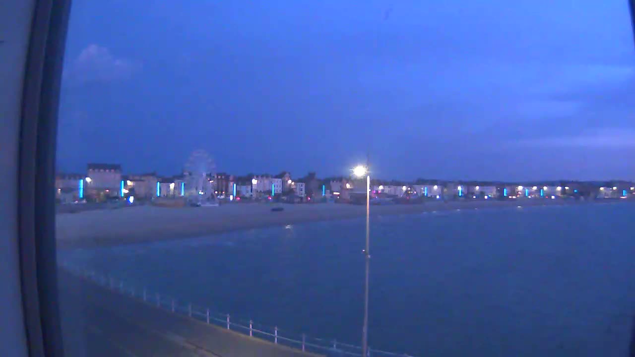 A seaside town at dusk, with a Ferris wheel visible on the beach, is seen from across a calm body of water.
