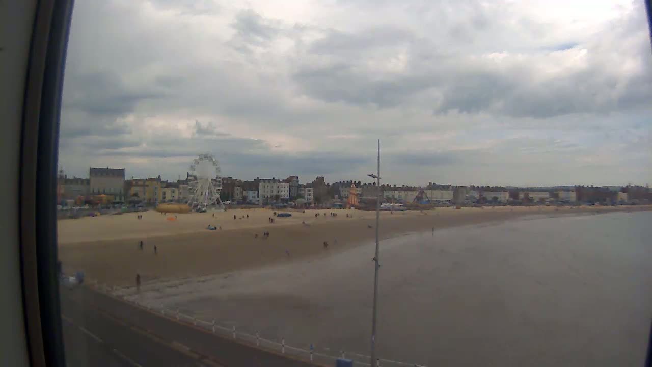 A sandy beach with a Ferris wheel and buildings in the background under a cloudy sky.