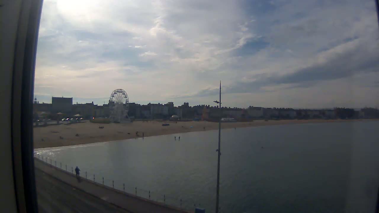 A mostly sunny day shows a beach with a Ferris wheel and buildings in the background, viewed from a pier.