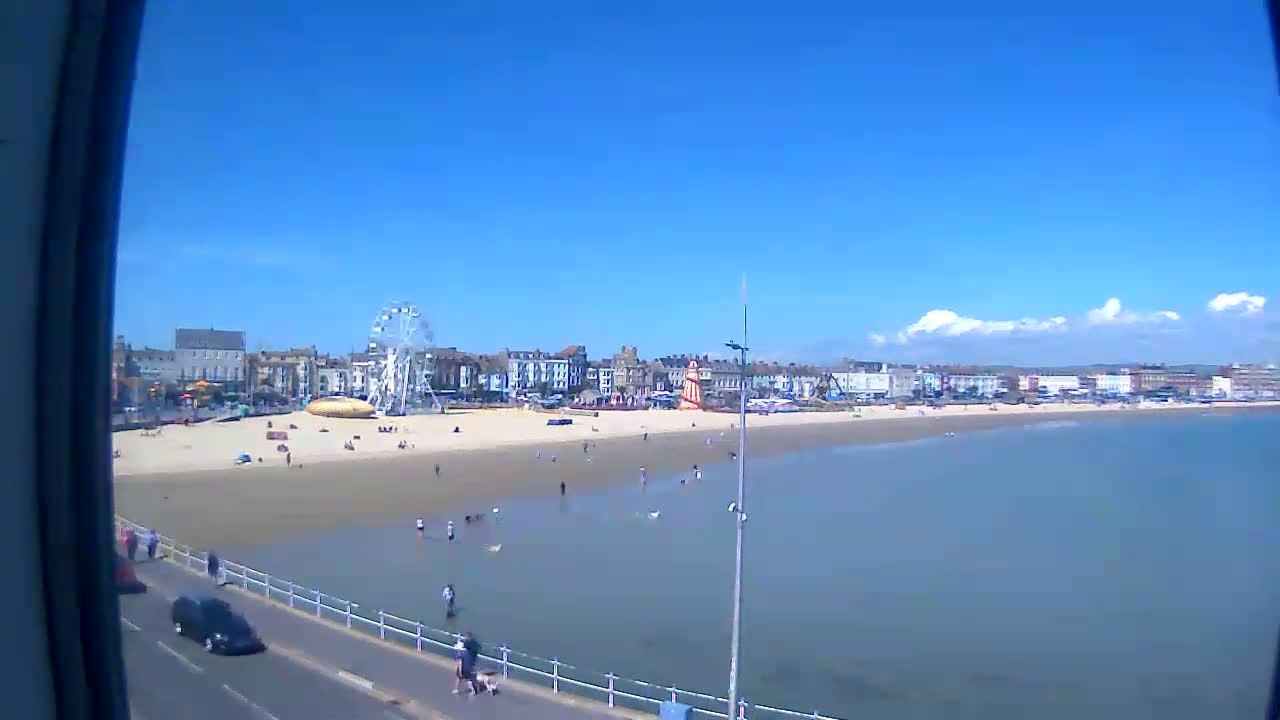 A sunny day at a beach with a Ferris wheel and several people enjoying the sand and shallow water.