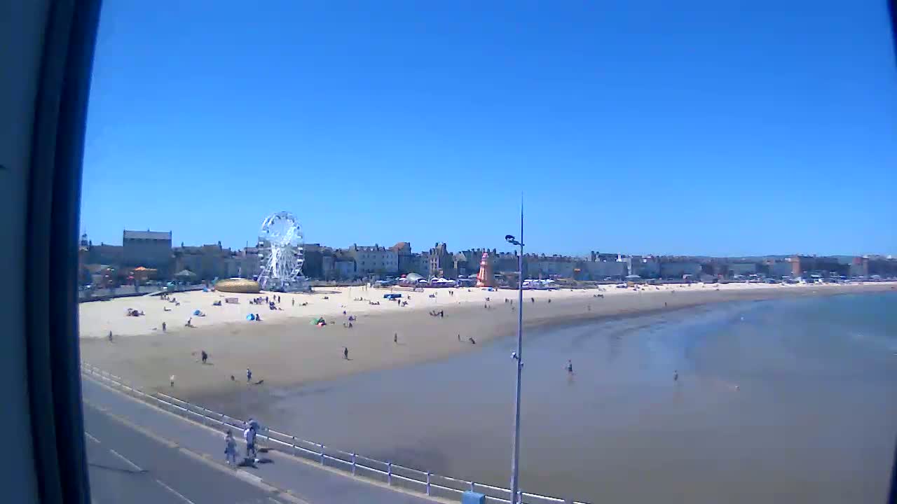A sandy beach with a Ferris wheel and several people is visible on a sunny day, with calm, shallow water extending out to the ocean.