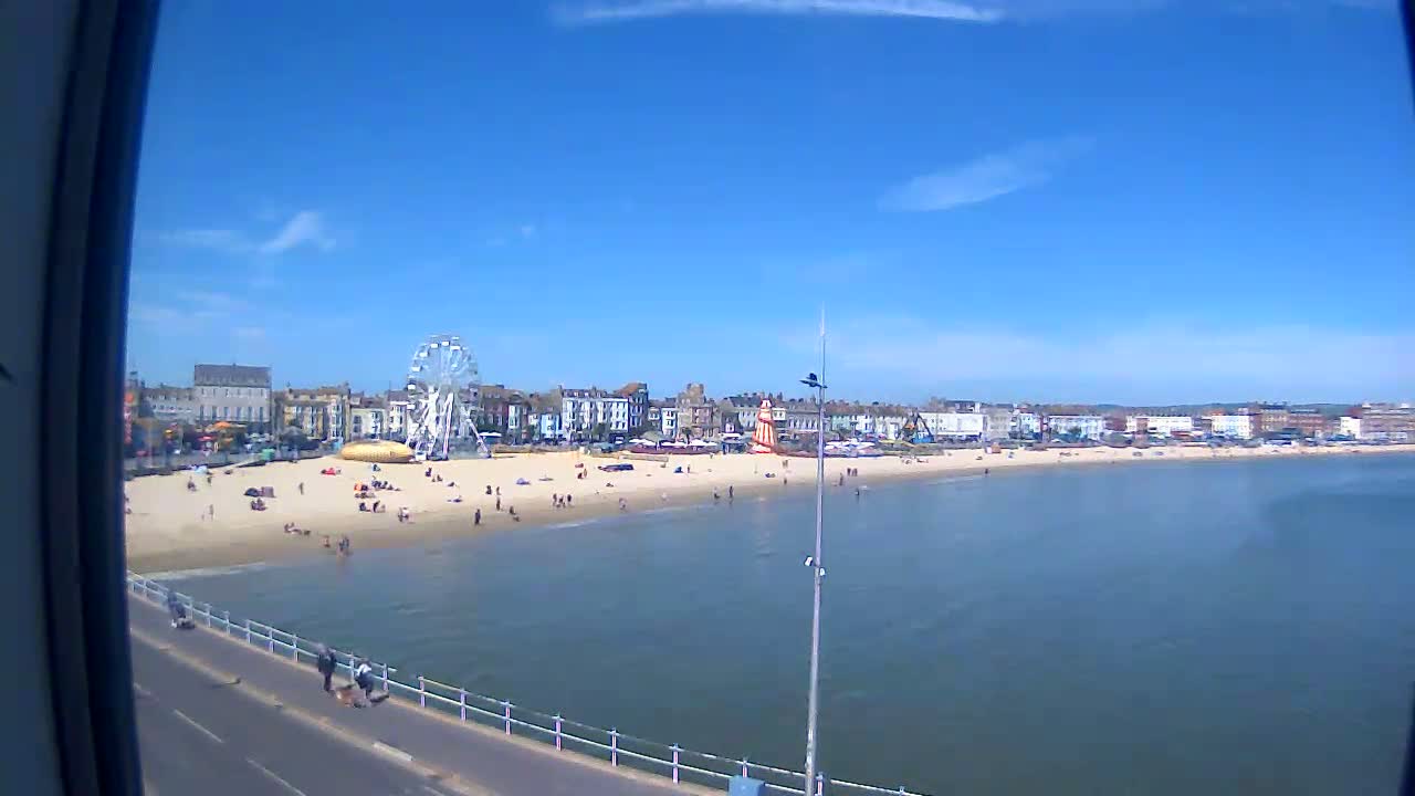 A sunny day at a beach with a Ferris wheel and many people enjoying the sand.