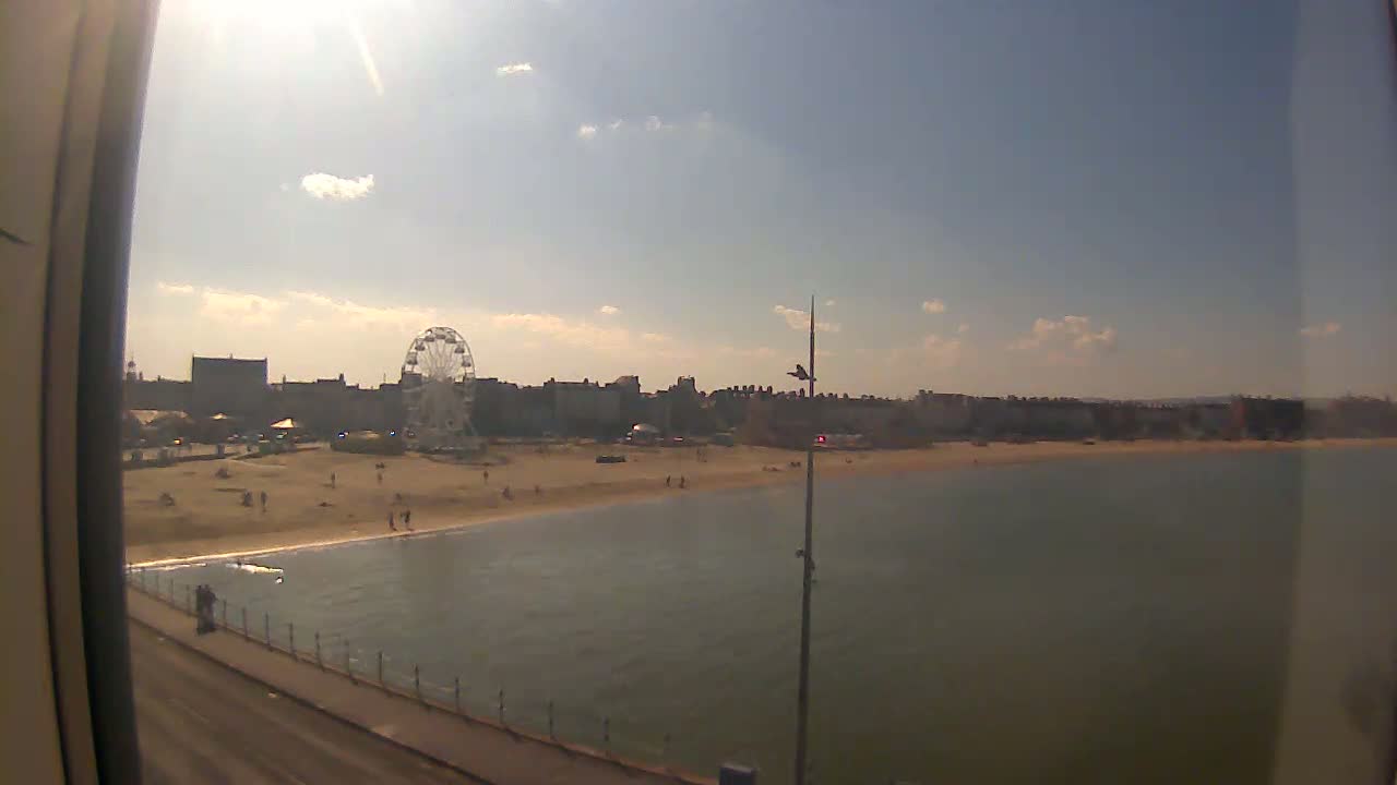 A sunny day reveals a beach with a Ferris wheel and buildings in the background, viewed from a pier.