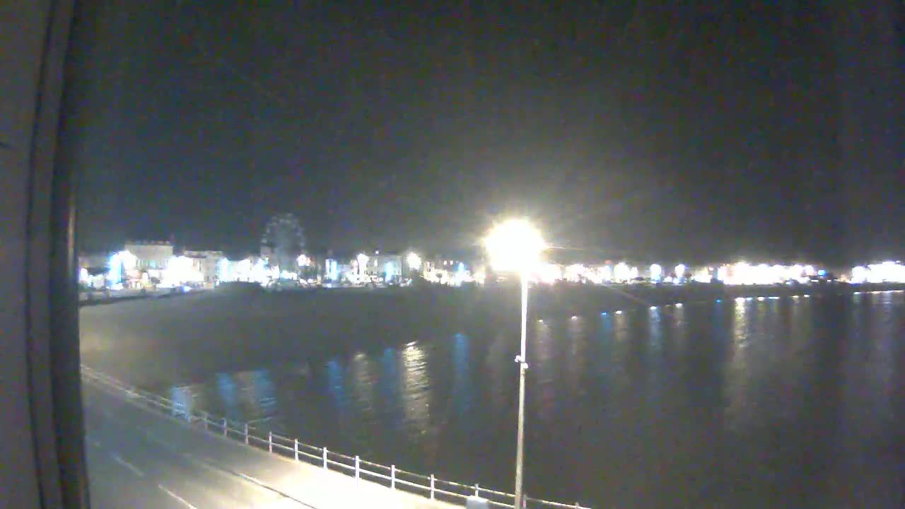 A nighttime view of a calm body of water reflecting the lights of a town across the water.