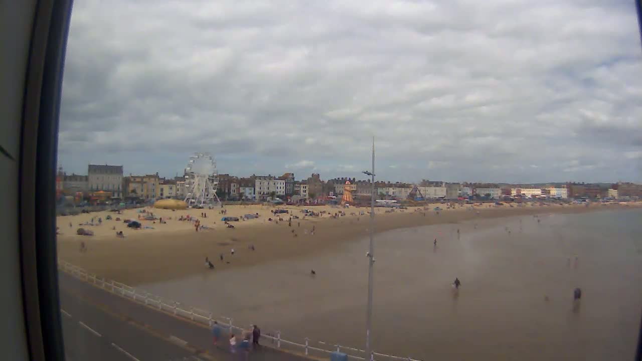 A sandy beach with a Ferris wheel and buildings in the background under a cloudy sky.