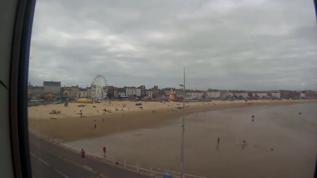 A sandy beach with a Ferris wheel and buildings in the background under an overcast sky.