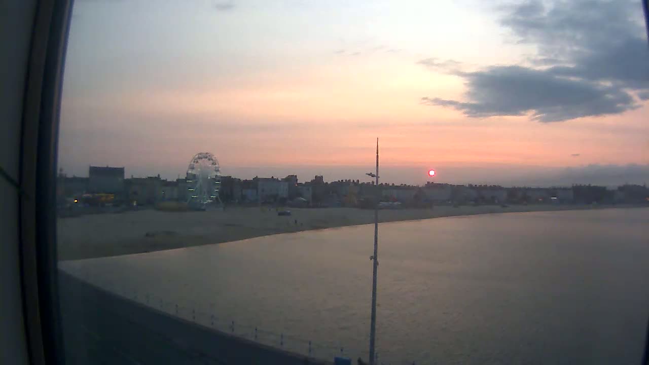 A beach with a Ferris wheel and buildings is visible at sunset over calm water.