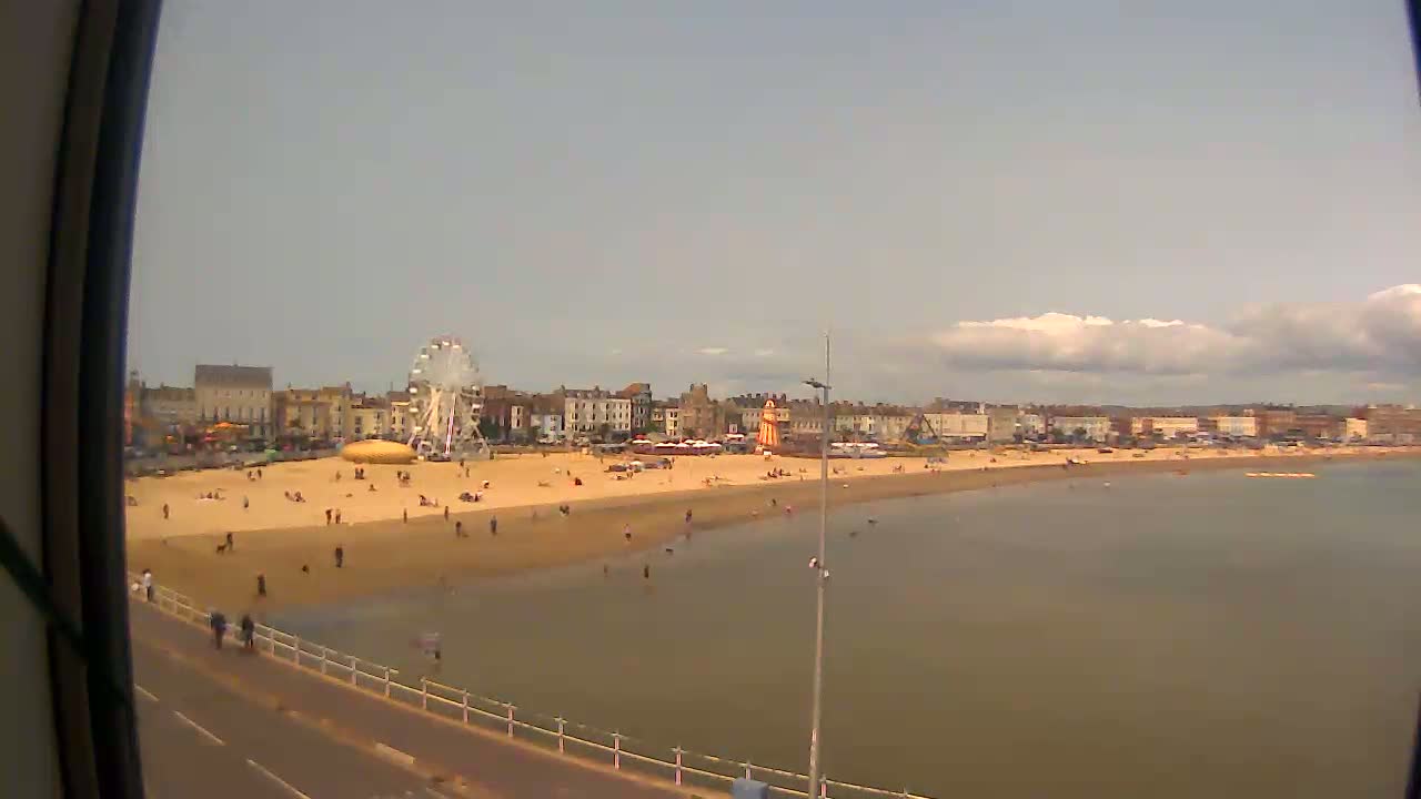 A sandy beach with a Ferris wheel and several buildings in the background is shown on a partly cloudy day.