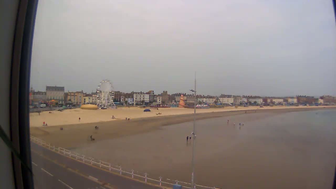 A mostly cloudy day shows a beach with a Ferris wheel and several buildings in the background, sparsely populated with people.