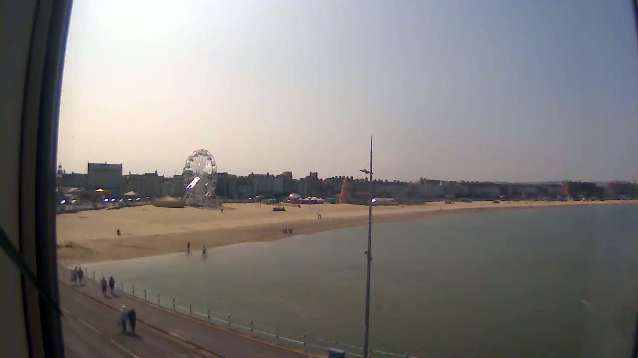 A sandy beach with a Ferris wheel and buildings in the background, on a sunny day, is partially visible through a window.