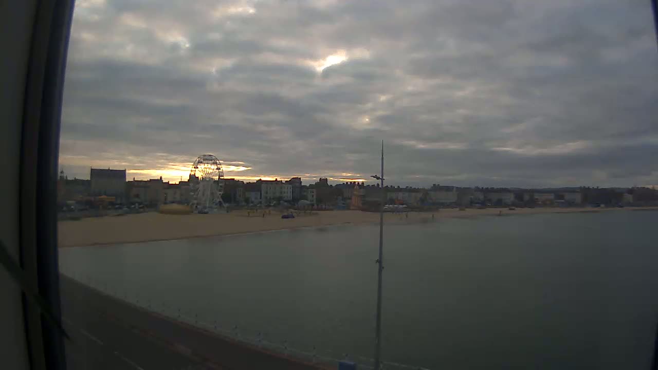 A Ferris wheel sits on a beach next to buildings under a cloudy sunset sky.