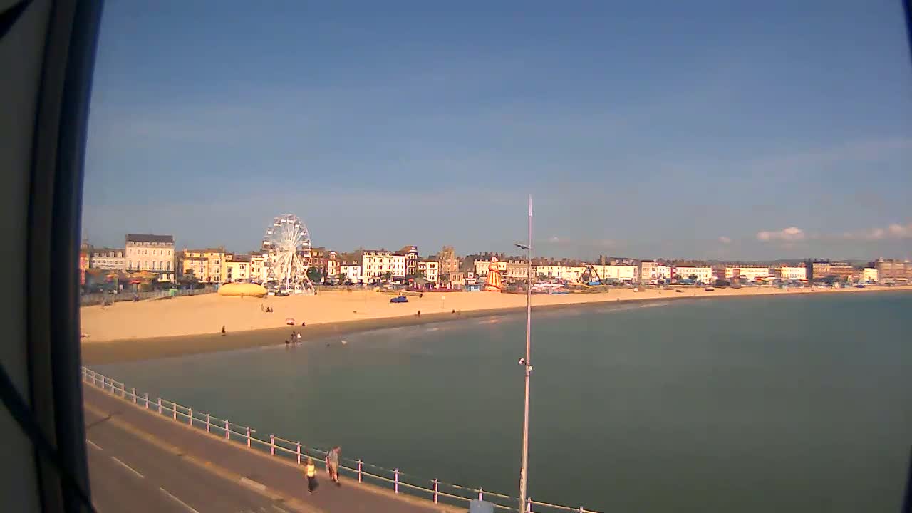 A sandy beach with a Ferris wheel and buildings in the background, under a clear blue sky.