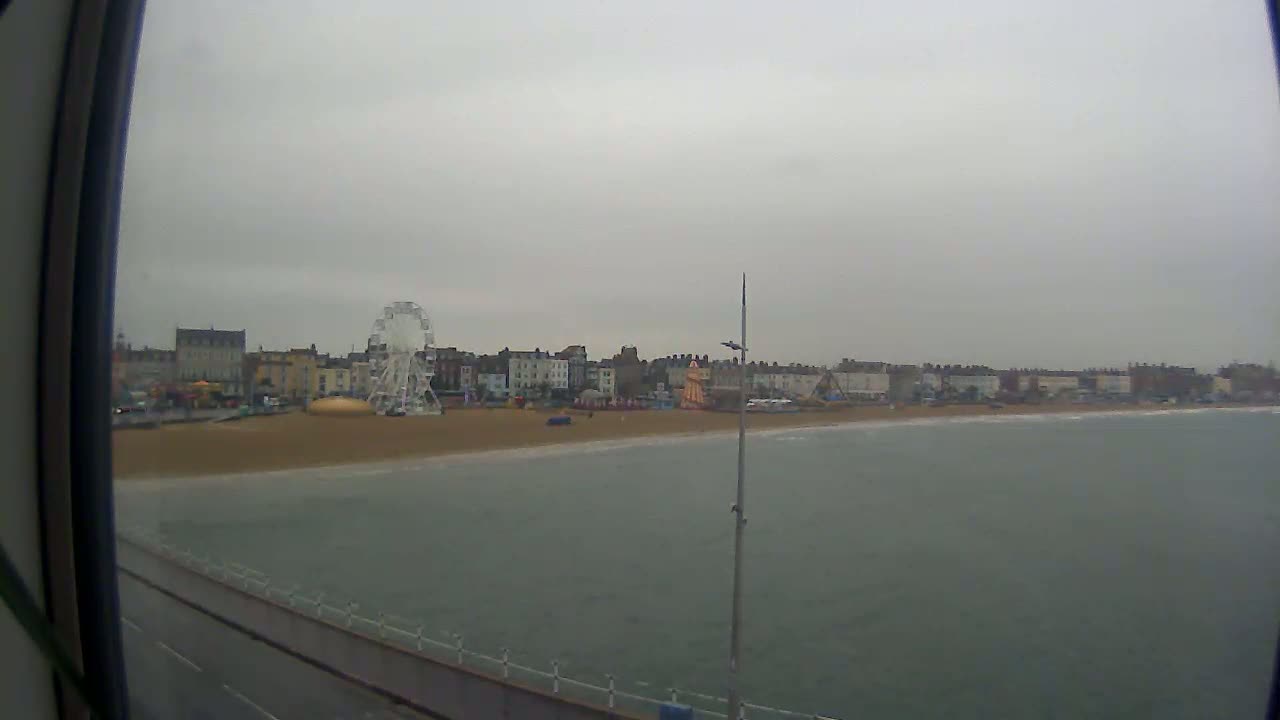 A Ferris wheel and beachfront buildings are visible across a calm, gray sea under an overcast sky.