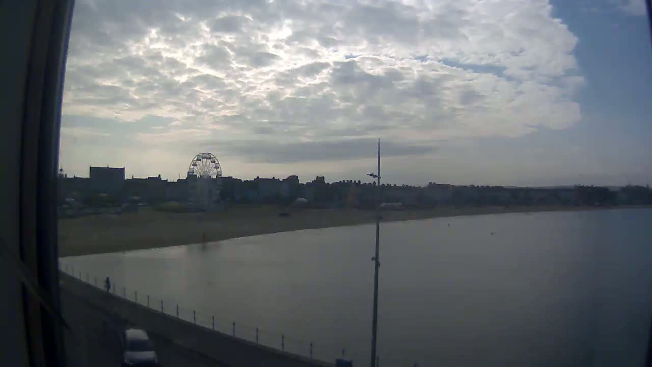 A beach with a Ferris wheel and buildings behind it is seen under a cloudy sky from what appears to be a window.