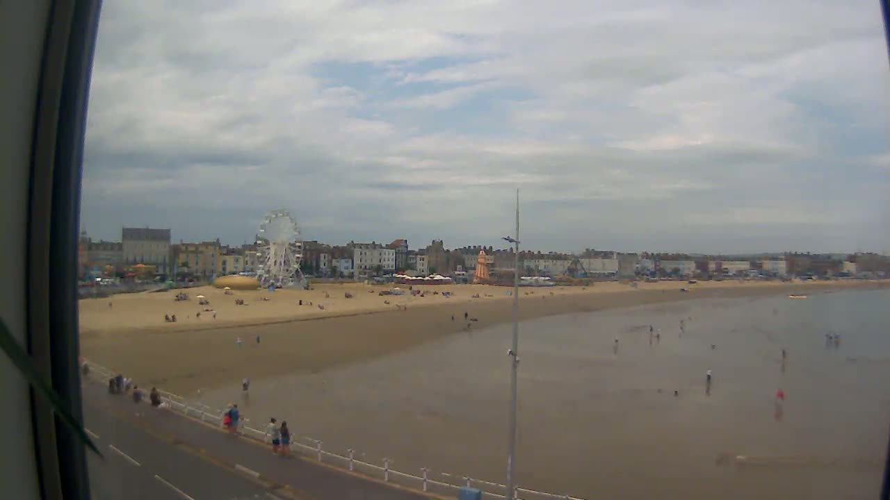 A sandy beach with a Ferris wheel and buildings in the background under a cloudy sky.