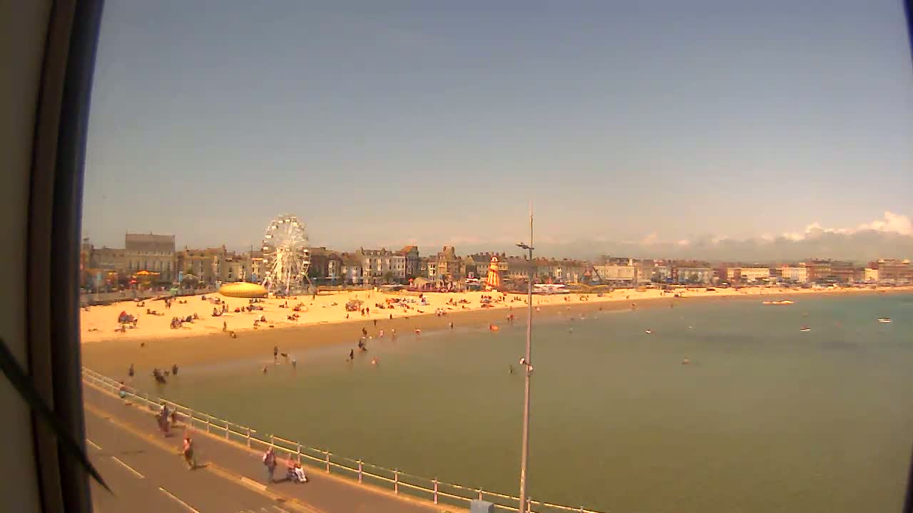 A sunny day at a beach with a Ferris wheel and many people enjoying the sand and shallow water.