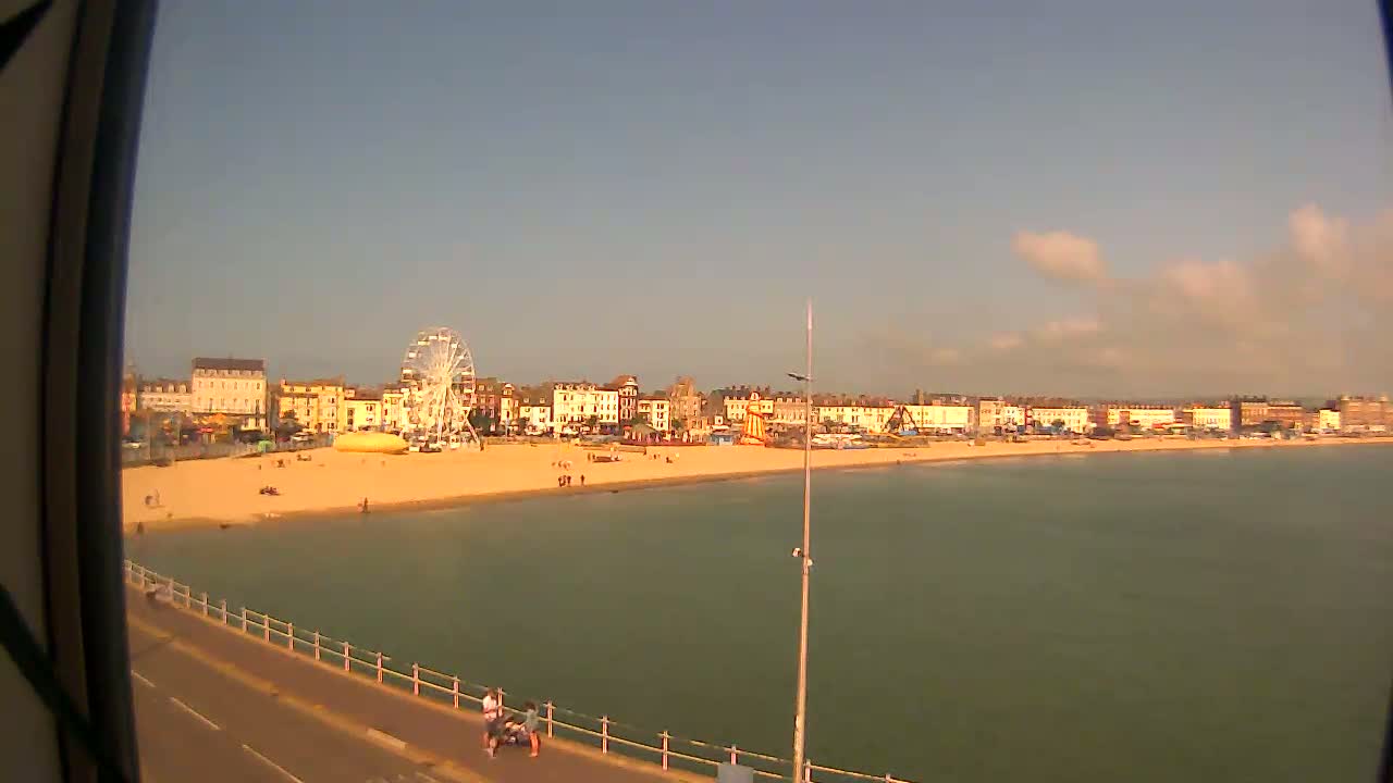 A seaside town with a Ferris wheel, beach, and calm water under a partly cloudy sky.
