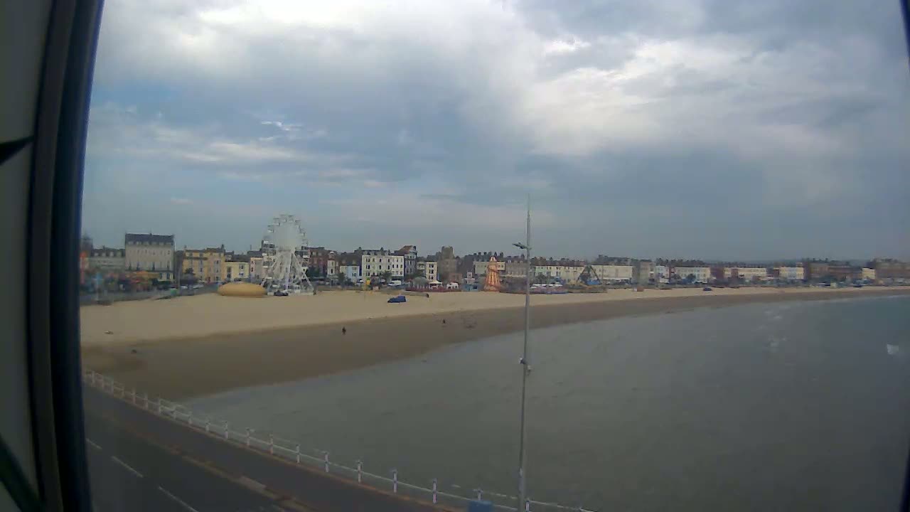 A sandy beach with a Ferris wheel and buildings behind it is viewed on an overcast day.