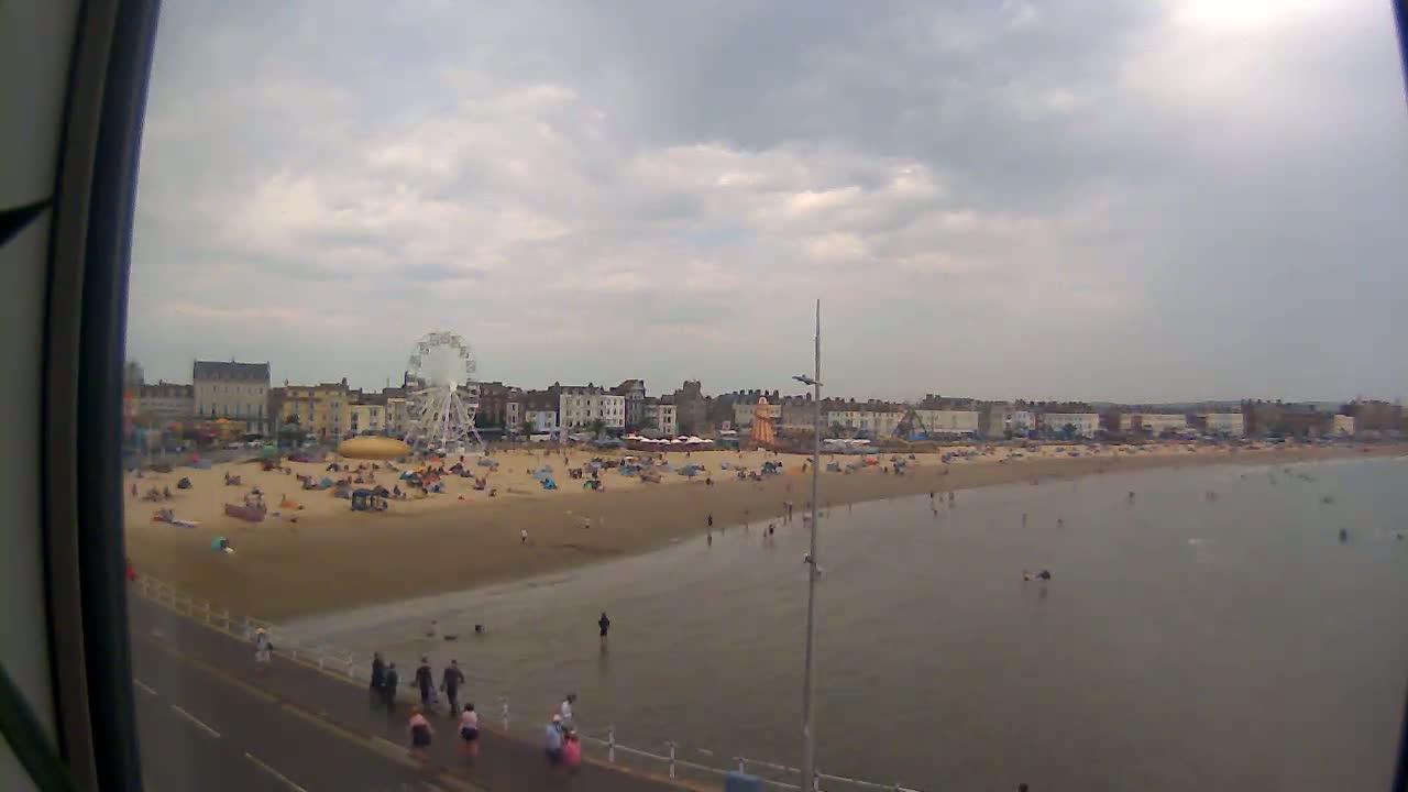 A crowded beach with a Ferris wheel and buildings in the background under an overcast sky.