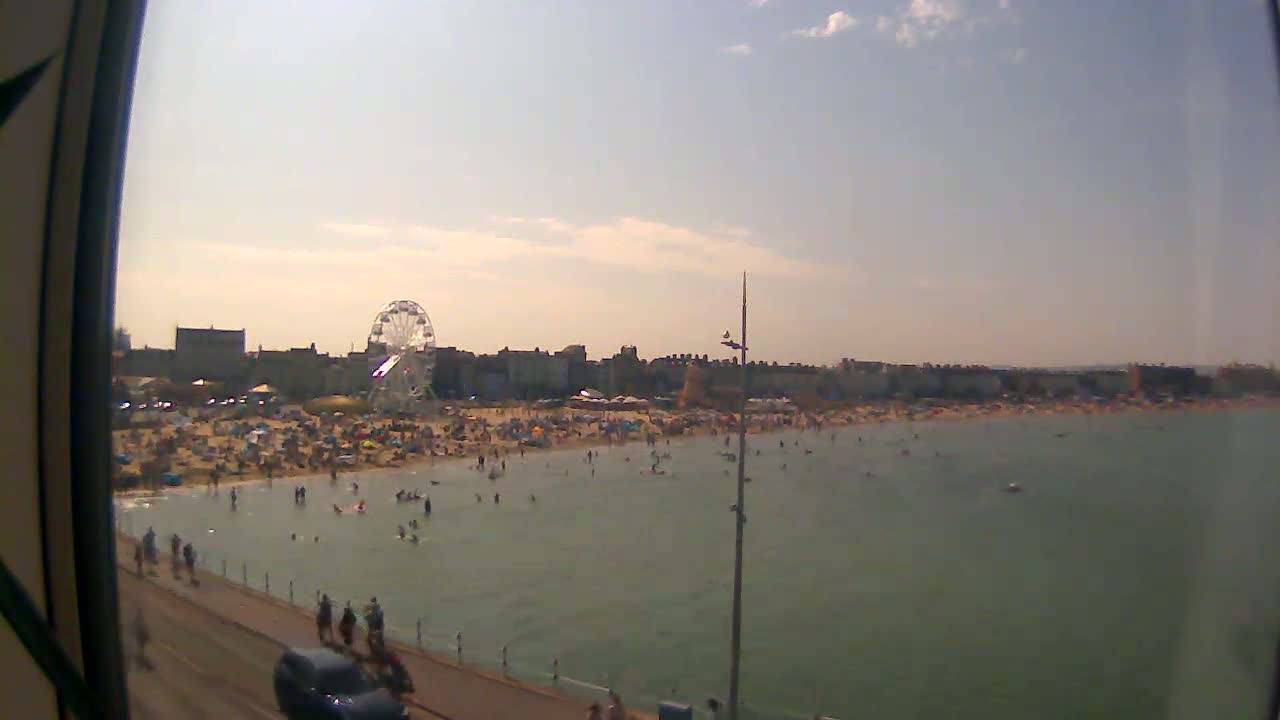 A crowded beach with a Ferris wheel in the background on a sunny day.