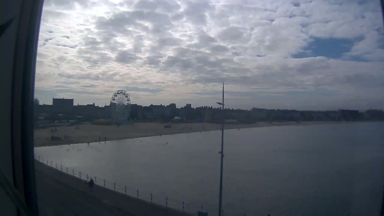 A mostly cloudy day reveals a beach with a Ferris wheel and calm, flat water.