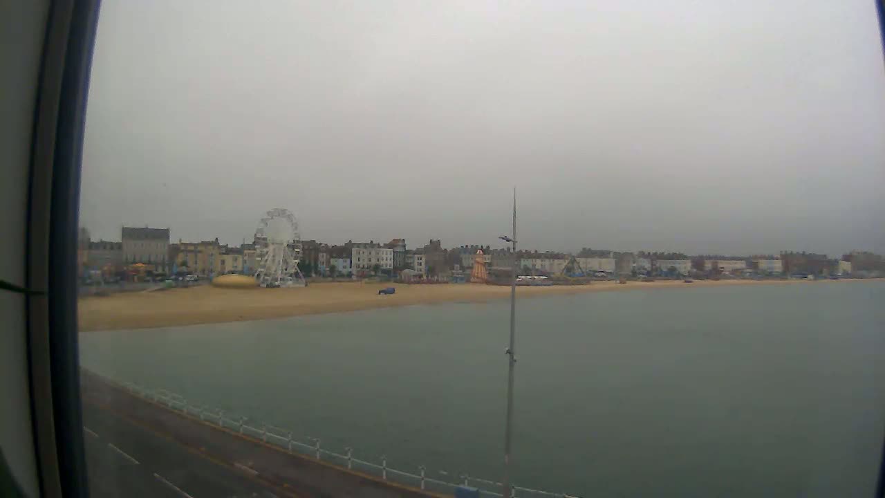 A beach with a Ferris wheel and buildings in the background is visible on an overcast day.