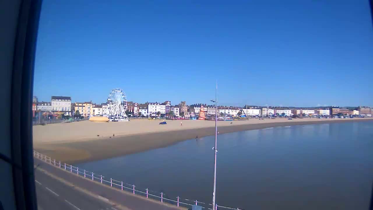 A Ferris wheel sits on a sandy beach next to a calm body of water, under a clear blue sky.