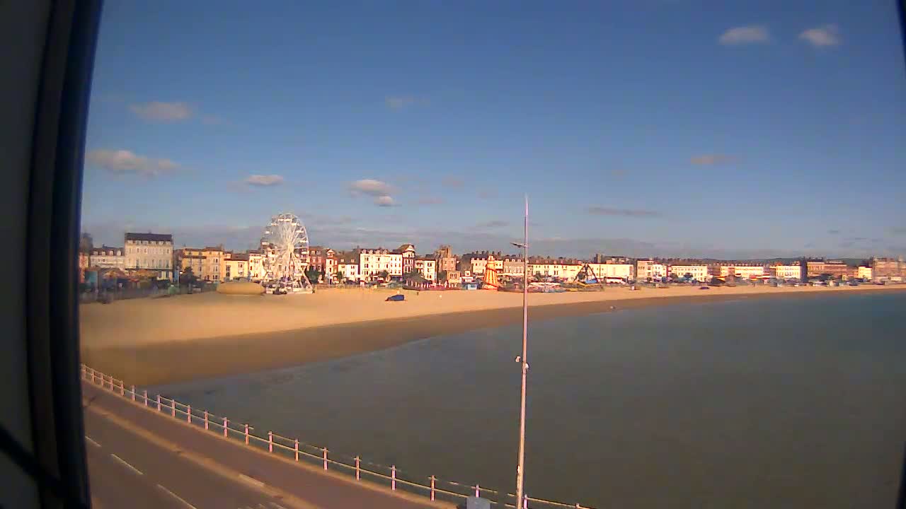 A sandy beach with a Ferris wheel and buildings behind it, viewed from a slight elevation on a partly sunny day.