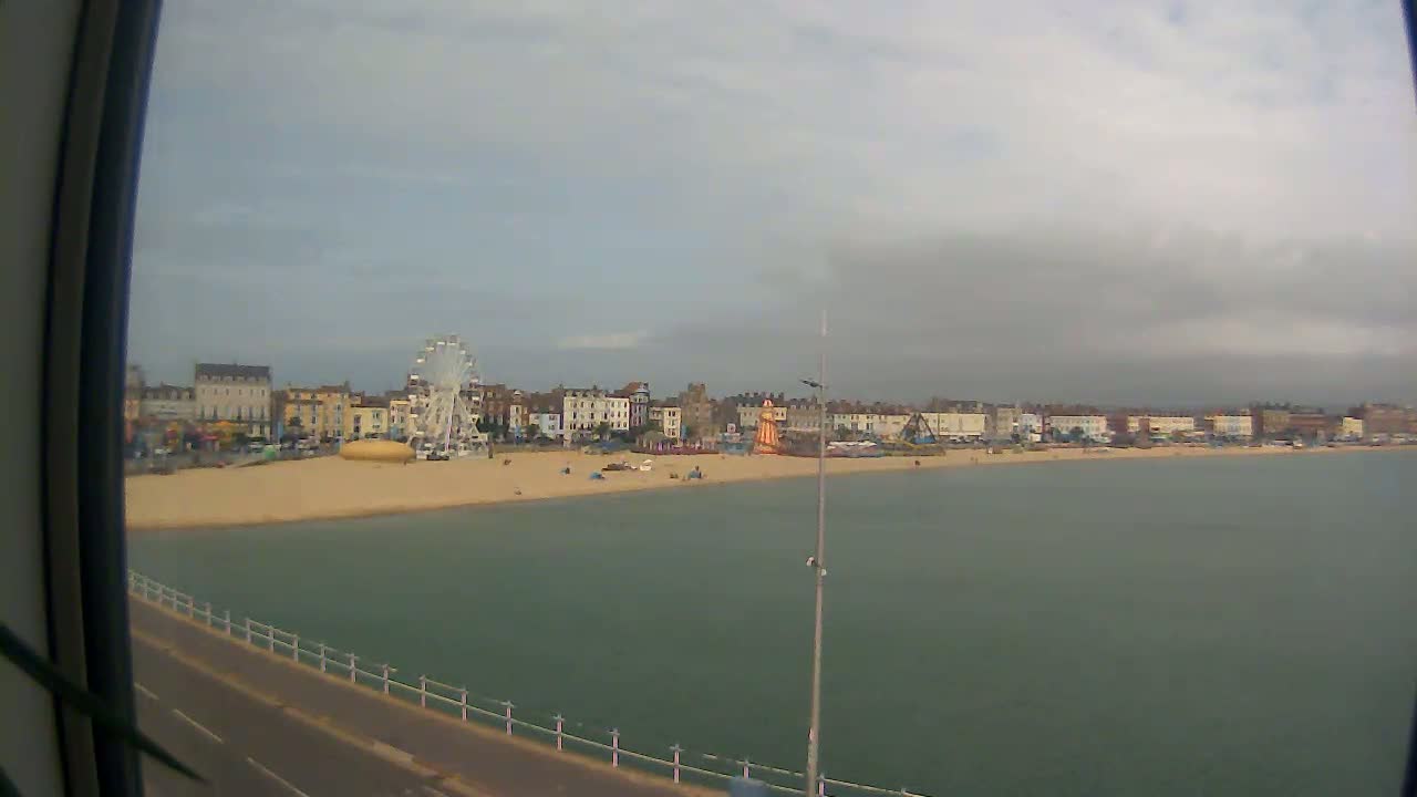 A sandy beach with a Ferris wheel and buildings along the shoreline is visible under an overcast sky.