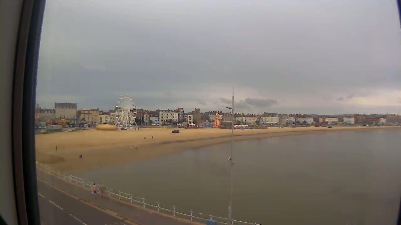 A sandy beach with a Ferris wheel and buildings behind it is seen under an overcast sky from a high vantage point.