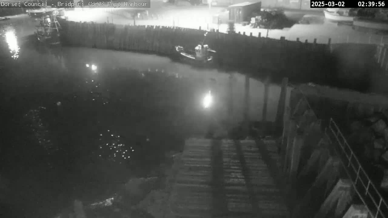 A nighttime, low-light view of a harbor with a small boat moored near a wooden wall, the water appearing calm.