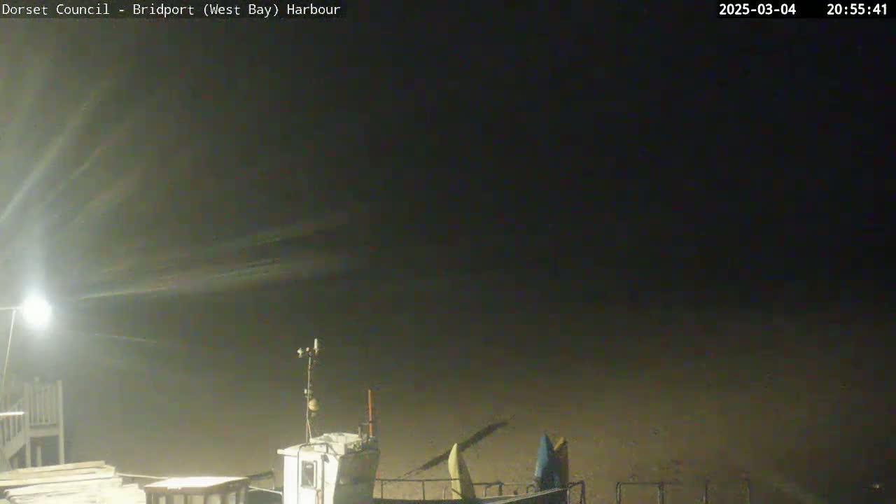 A nighttime harbor scene shows a boat docked at a dimly lit pier under a dark, hazy sky.