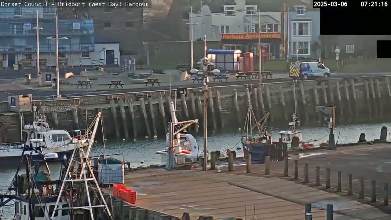 A harbor with several boats, a small crane, and buildings along the waterfront on a partly cloudy morning.