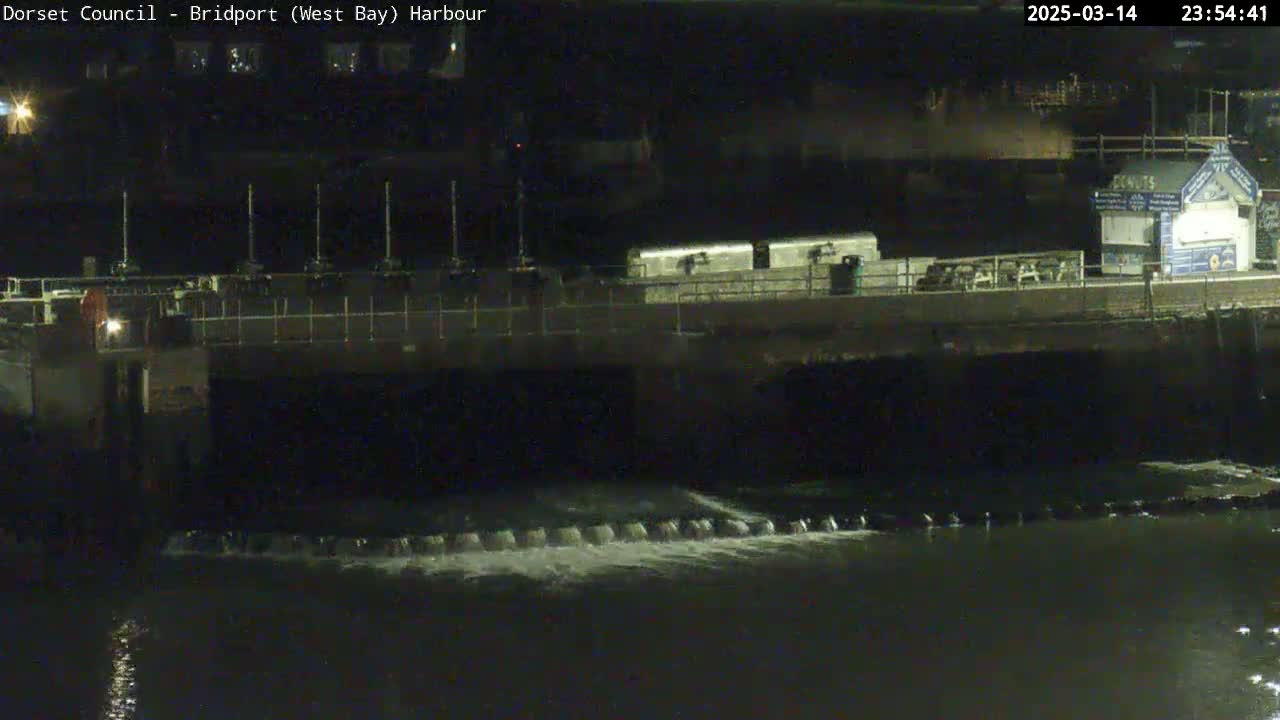 A nighttime view of a harbor with water flowing over a dam under a dark sky.