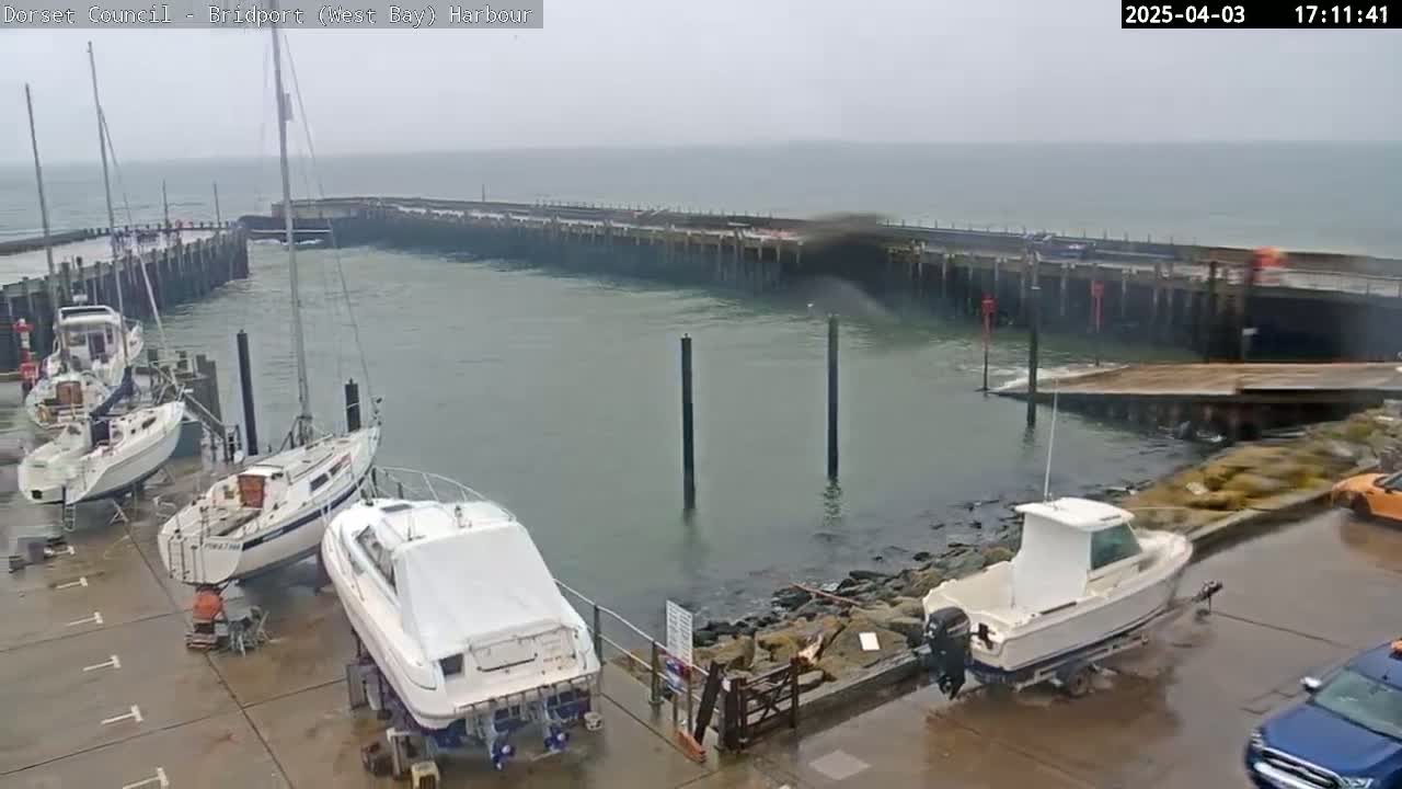 Several boats are docked at a harbor on a cloudy day, with some boats on trailers and others in the water.