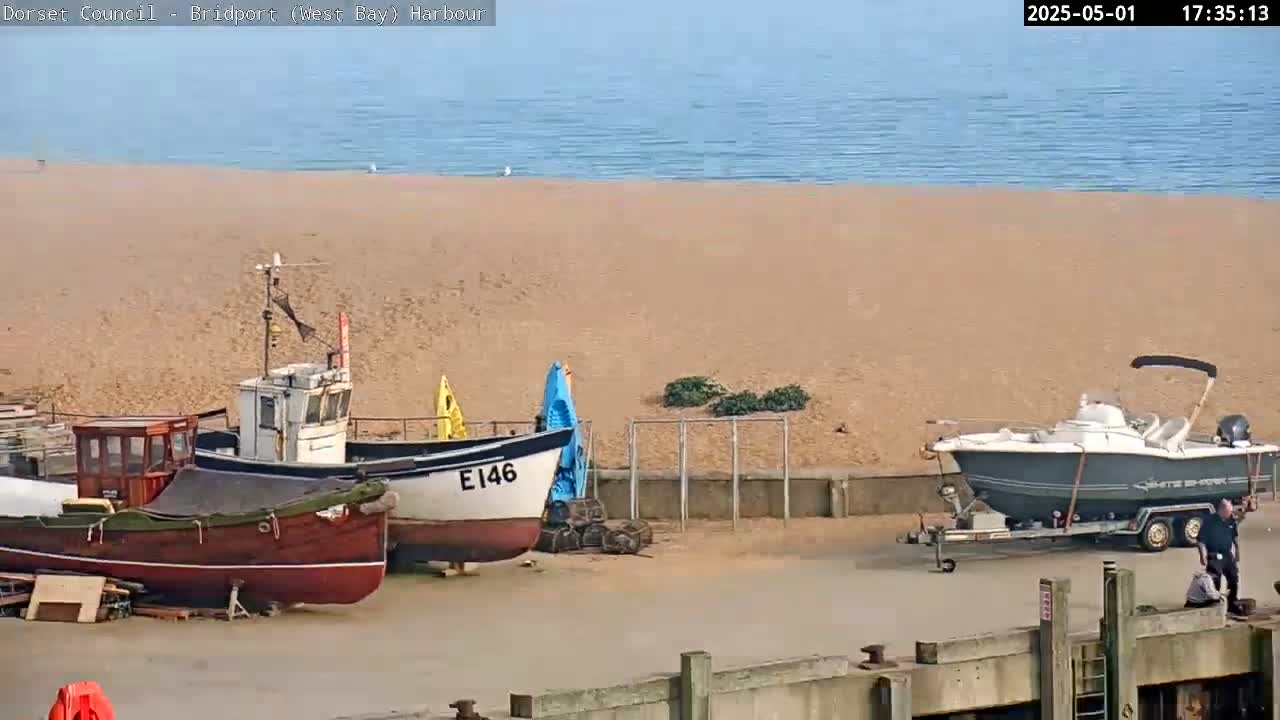 Several small boats are docked near a sandy beach with calm, blue-grey water visible in the background under a clear sky.