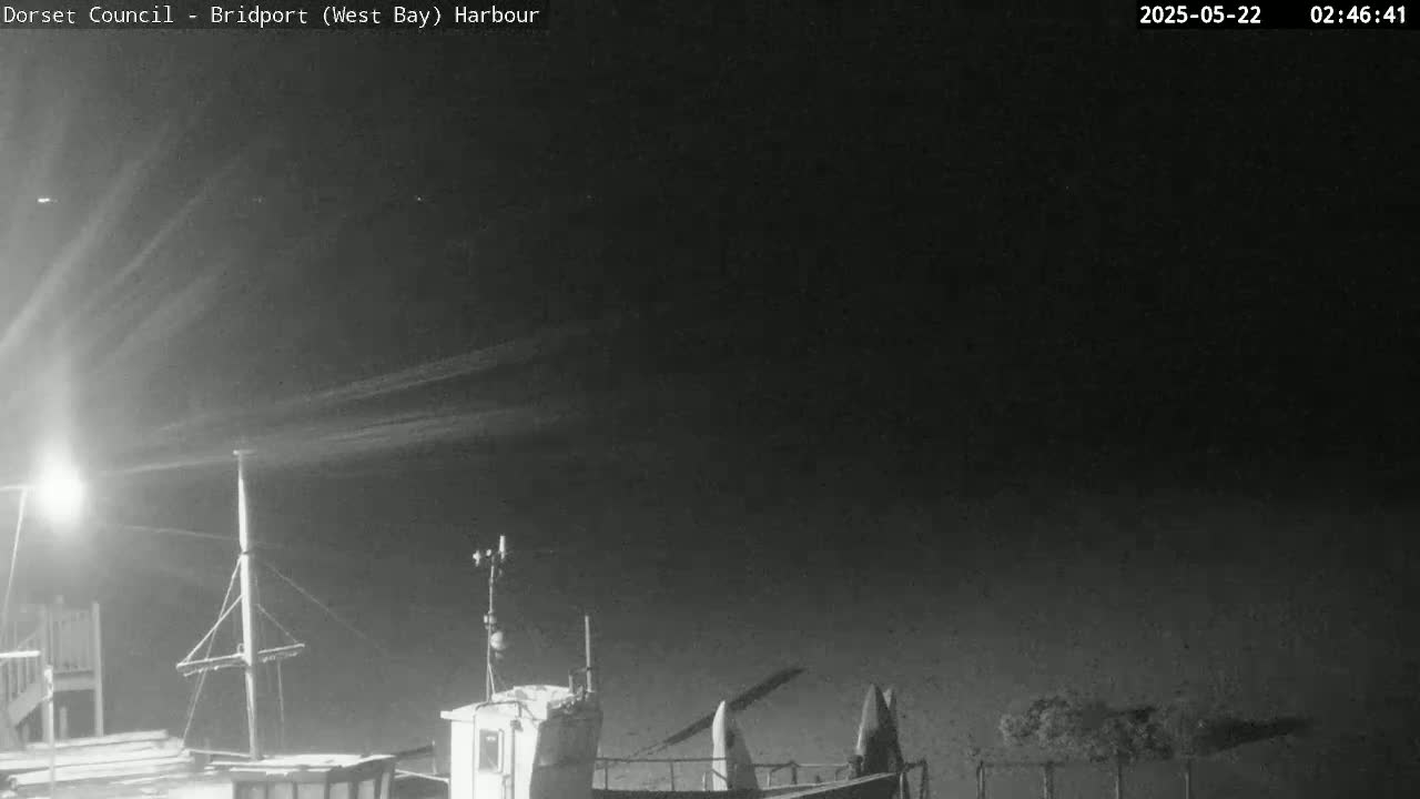 A nighttime harbor scene shows a boat docked under a dark sky with light streaks possibly from airplanes or satellites.