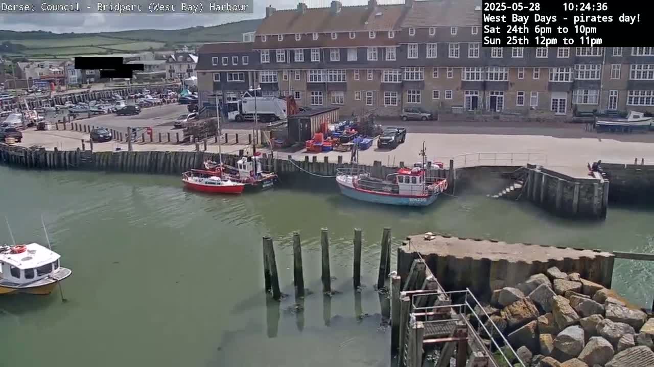 Several small boats are moored in a harbor next to a multi-story building under a sunny sky.