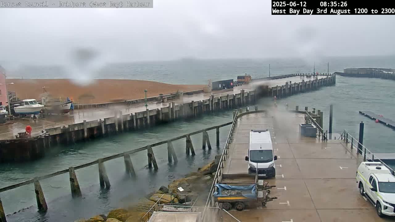 A harbor scene in overcast weather shows a pier and boats, with several vehicles parked on the dock.